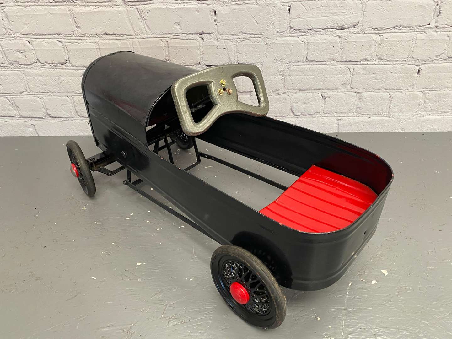<p>A mid 20th century pressed steel pedal car,&nbsp;</p>